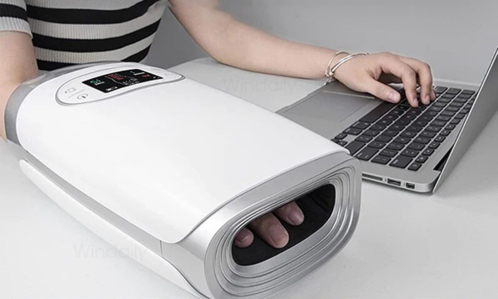 Woman using the Alevez HandBliss hand massager while working at a laptop, according to the brand
